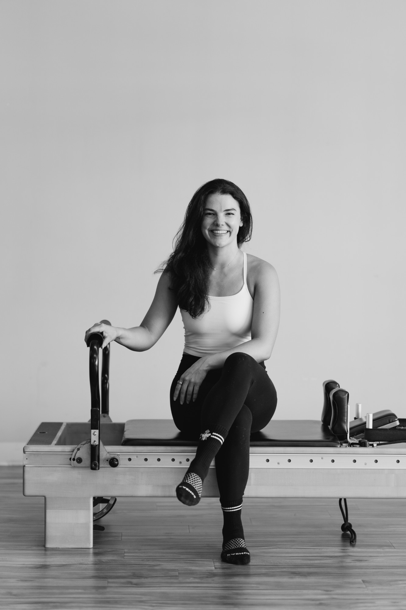 Black-and-white photo of Brett smiling, sitting on the edge of a reformer