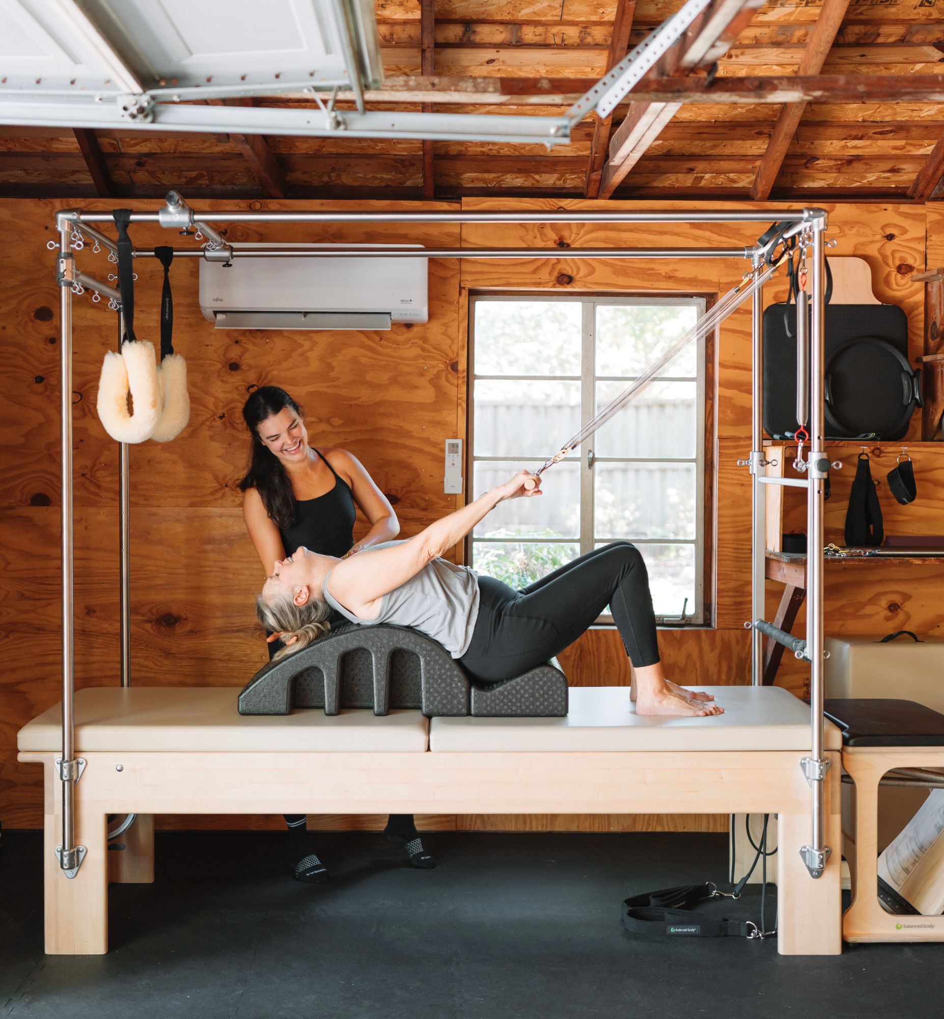 Brett laughing with a client during a Pilates session on the Cadillac in her home studio
