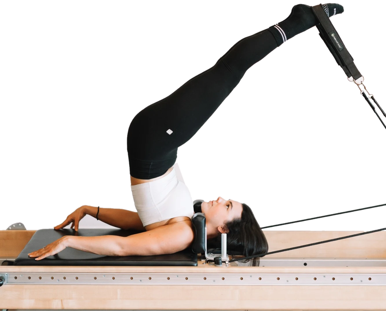 Brett on a reformer, legs lifted overhead in the foot straps