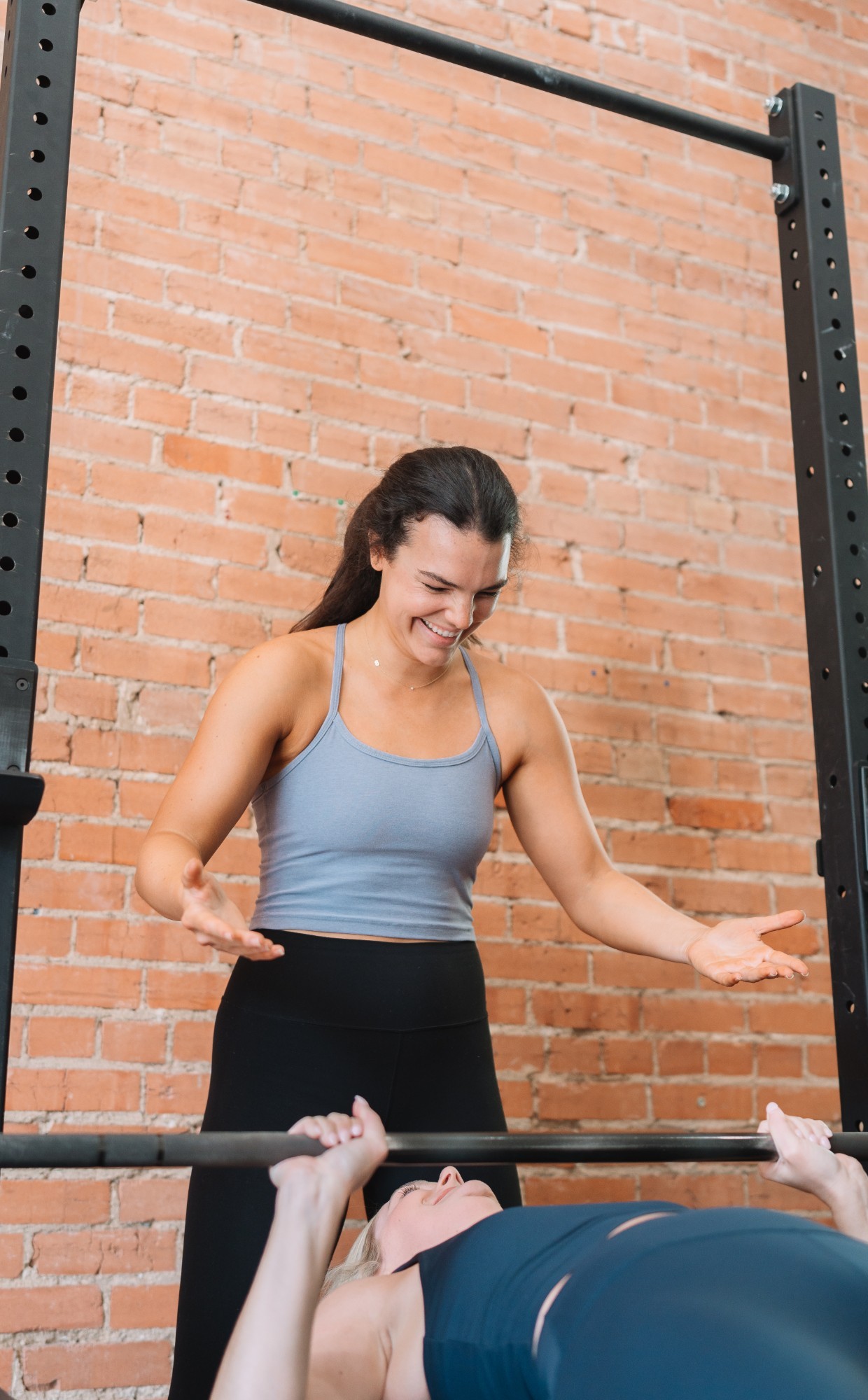 Brett smiling as she spots a client pressing a barbell on the bench