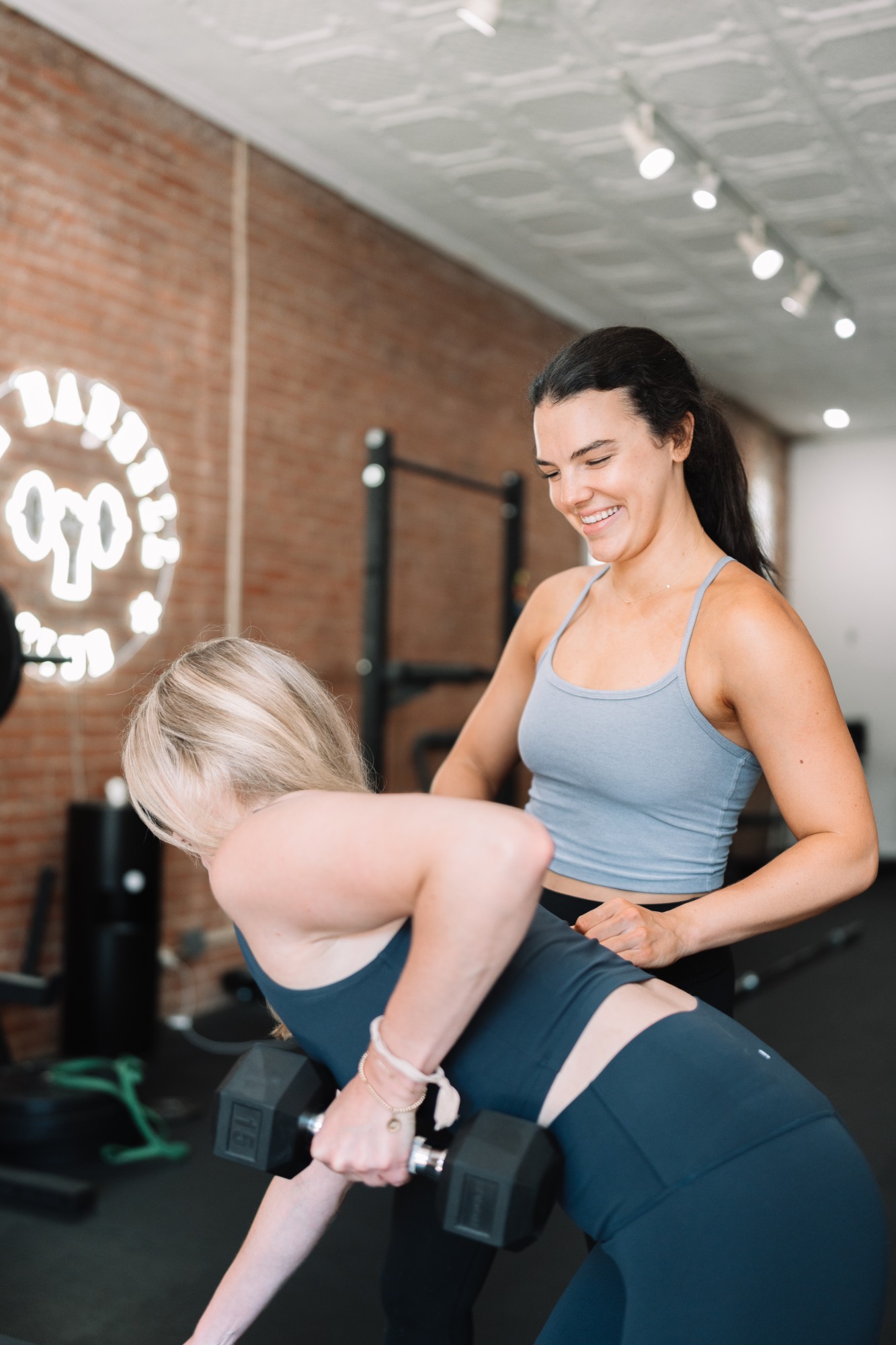 Brett smiling as she guides a client through a dumbbell row