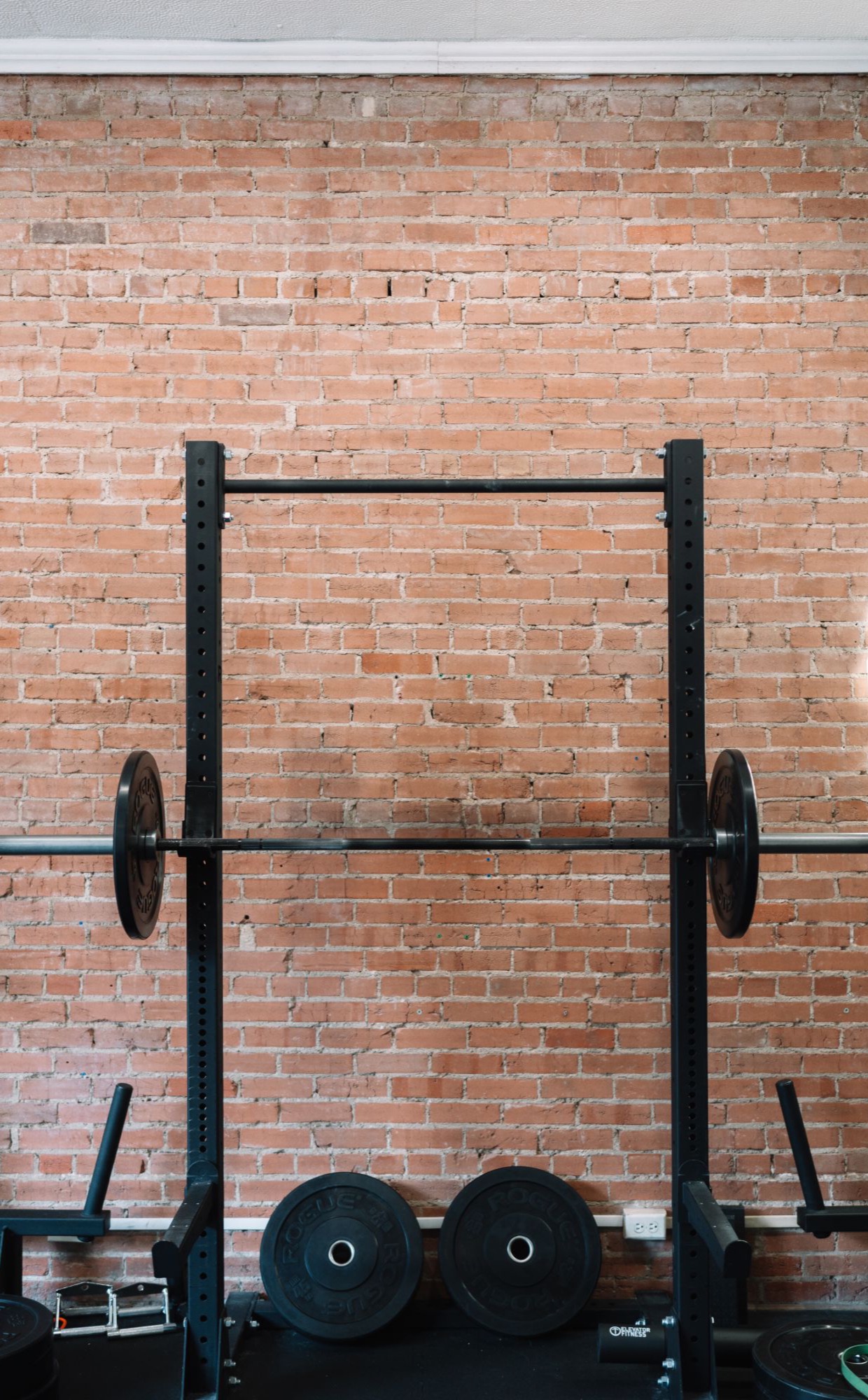 A squat rack with a loaded barbell against a brick wall